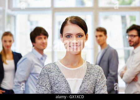 Entreperneur giovane donna in piedi e sorridente nella parte anteriore del team di successo Foto Stock