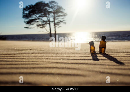 Essenziale olio di pino sulla sabbia al tramonto con un bellissimo spazio copia - Mare e albero in background. Concetto vantaggio, energia di oli naturali. Foto Stock