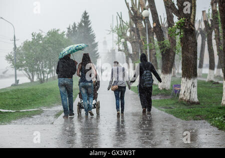 Gruppo di persone a piedi giù per la strada di heavy rain in motion blur. Concetto di cattive condizioni atmosferiche, resistenza alle difficoltà. Foto Stock