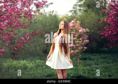 Bella ragazza bionda in rosa pesca e sakura garden. Femmina a molla esterno ritratto, giovane donna con al verde parco blossom concept Foto Stock