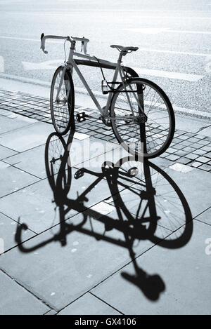 Hipster singolo ingranaggio fixie bicicletta bloccato ad un supporto metallico su un marciapiede. Grande ombra proiettata sul marciapiede. Foto Stock