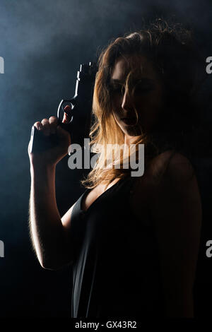 Donna in possesso di una pistola nel buio Foto Stock