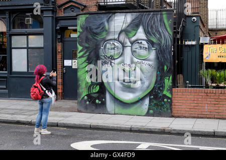 Una donna con i capelli rossi fotografie un ritratto di John Lennon. Foto Stock