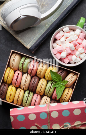 Amaretti colorati in una confezione regalo e le cuffie sul tavolo di pietra. Dolce macarons. Vista superiore Foto Stock