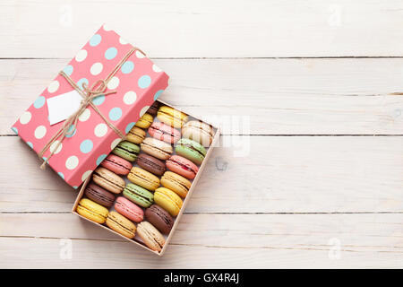 Amaretti colorati su un tavolo di legno. Dolce macarons in confezione regalo. Vista da sopra con copia spazio per il testo Foto Stock