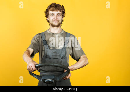 Bello sorridente meccanico mantiene la ruota giallo Foto Stock