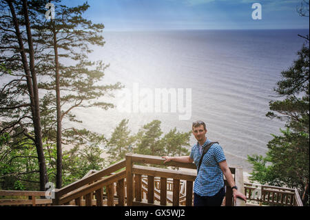 Giovane uomo seduto sulle scale di legno nel parco e sorridente Foto Stock