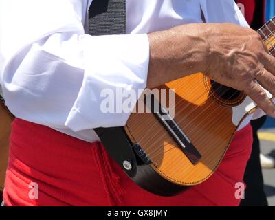 Close up di un canarino Islander indossando costumi regionali con colore rosso brillante anta, riproduzione di un 'timple', un tradizionale ukelele-come strumento Foto Stock