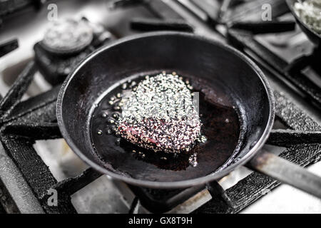 Red bistecca di tonno in crosta con il bianco e nero di semi di sesamo essendo fritti in olio di oliva in padella Foto Stock