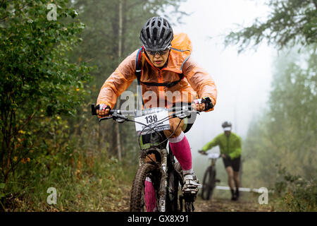 Primo piano della donna racer ciclista scorre attraverso la foresta durante gare regionali su cross-country Foto Stock