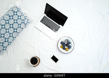 Lavorando a letto , laptop e la tazza di caffè sul letto bianco, la luce del mattino Foto Stock