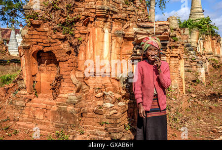 Vecchia donna rugosa fuma un sigaro cheroot intorno templi in rovina nella città antica di Ava, chiamato anche Inwa Foto Stock