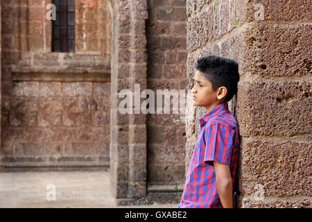 Teenage moody boy appoggiata contro il vecchio rosso muro di mattoni Foto Stock