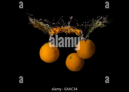 Tre arance in acqua sollevata una grande onda su sfondo scuro Foto Stock