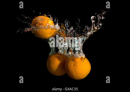 Tre arance in acqua sollevata una grande onda su sfondo scuro Foto Stock