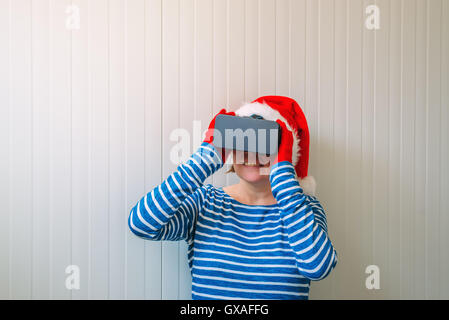 Donna con il Natale di Santa Claus hat e VR occhiali cuffia godendo 360 visualizza il video e la realtà virtuale di contenuti multimediali. Foto Stock