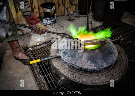 Fonderia maschio lavoratore riscaldamento lingotto di bronzo al di sopra del forno in fonderia di bronzo Foto Stock