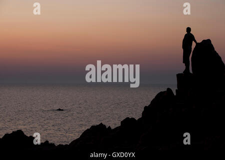 Silhouette di uomo sulle rocce guardando l'oceano al tramonto, Capo Testa, Gallura Sardegna, Italia Foto Stock