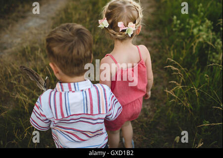 Vista posteriore del giovane ragazza e fratello gemello tenendo le mani in Prato Foto Stock