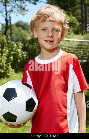 Close up ritratto di ragazzo indossa uniformi di calcio tenendo palla calcio in giardino Foto Stock