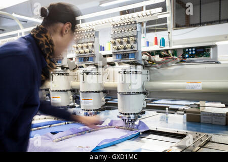 Femmina operaio di fabbrica la preparazione di panno per velocità programmata di cucitura della macchina da ricamo in fabbrica di abbigliamento Foto Stock