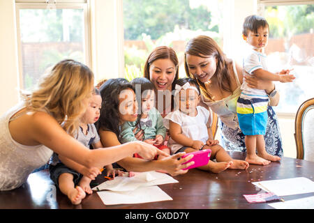 Donna prendendo selfie con le madri e i bambini al tavolo da pranzo Foto Stock