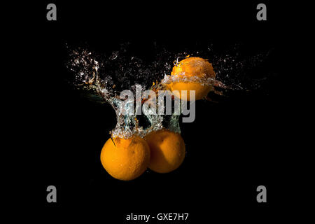 Tre arance in acqua sollevata una grande onda su sfondo scuro Foto Stock
