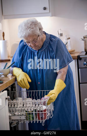 Gli anziani indipendenti lady concentrandosi sul suo carico lavastoviglie nella sua casa moderna cucina Foto Stock