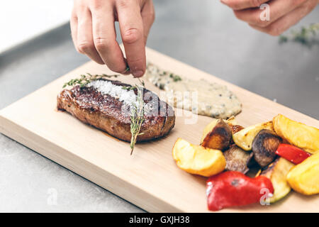 Lo chef serve la bistecca di manzo con salsa di senape e verdure grigliate Foto Stock