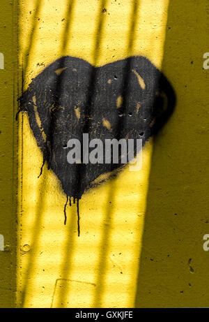 Cuore scuro dipinto sul muro con la vernice a spray. Le ombre create dai raggi del sole è simile dietro le sbarre di una prigione Foto Stock