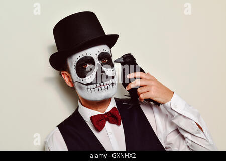 Un uomo con calaveras trucco, indossando gilet, il filtro bow tie e top hat, con un corvo nero nella sua spalla Foto Stock