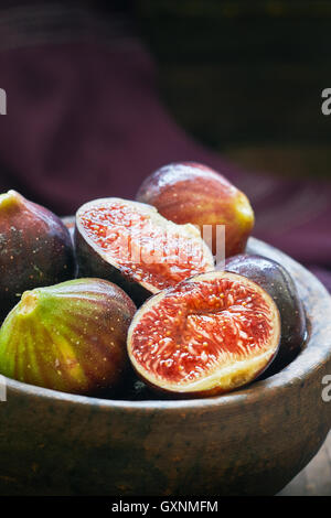 Fresche e mature figure nere nel recipiente rustico con sfondo viola. Spazio di copia Foto Stock