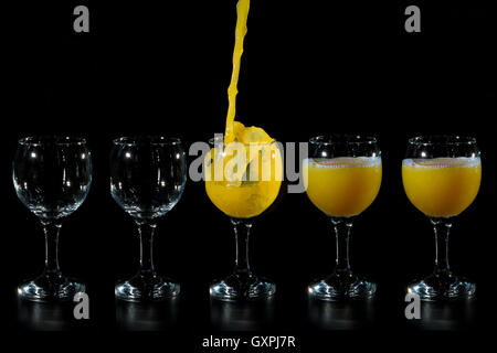 Getto di succo di arancia di essere versata in uno dei cinque coppa di vetro su uno sfondo nero Foto Stock