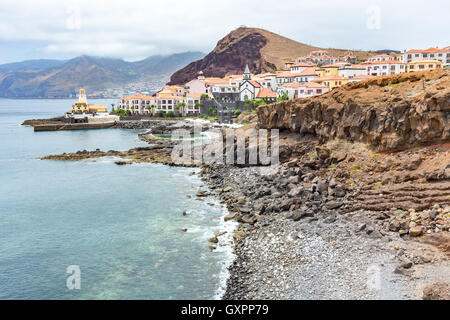 Costa in Madeira Mare con spiaggia sassosa montagne e villaggio con case Foto Stock