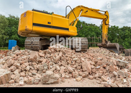 Nastro giallo escavatore sul mucchio di mattoni della demolita casa Foto Stock