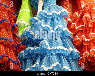 Close up tradizionale blu, rosso, verde e arancione frilly abiti di flamenco con macchie bianche e pizzo appeso a una fila Foto Stock