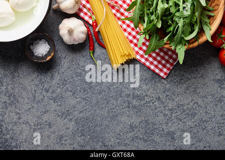 Il cibo italiano ingredienti sfondo con materie di spaghetti, insalata di rucola, mozzarella, peperoncino, aglio, sale e pomodori Foto Stock