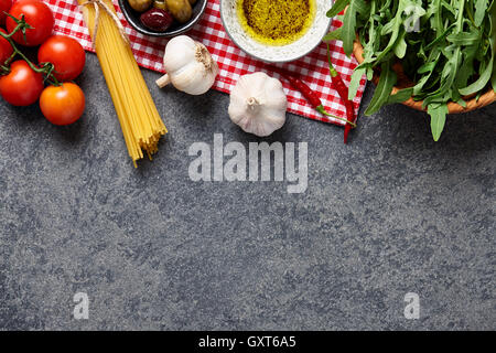Il cibo italiano ingredienti sfondo con materie spaghetti, olive, insalata di rucola, aglio, olio di oliva e pomodori. Foto Stock