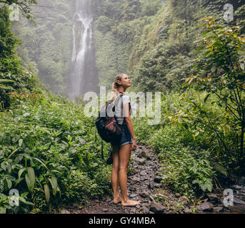 Bella donna escursionista in piedi sul sentiero forestale e guardando lontano. Femmina con zaino per escursioni nella natura. Foto Stock