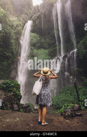 Vista posteriore del colpo di turista femminile ammirando bella cascata nella foresta pluviale tropicale. Giovane donna che guarda la cascata. Foto Stock