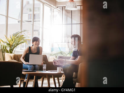 Colpo di due imprenditori seduti in ufficio a parlare della lobby e sorridente. Donna con notebook discutere idee di business con maschio co Foto Stock