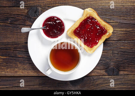 Toast con marmellata e tazza di tè scuro su un tavolo di legno. Vista superiore Foto Stock