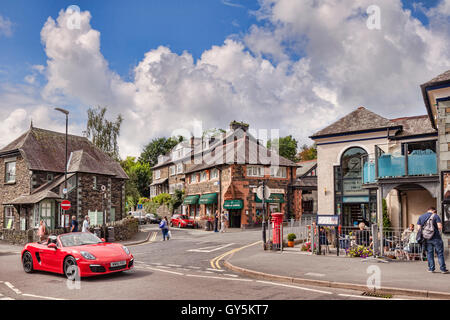 Un rosso sports car guida attraverso il villaggio di Ambleside, Parco Nazionale del Distretto dei Laghi, Cumbria, England, Regno Unito Foto Stock