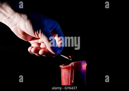 Mano umana con un fiammifero accende un cero rosso su sfondo nero Foto Stock