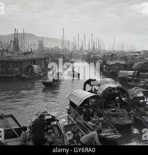 Anni '50, storico, una vista da questa epoca attraverso il villaggio galleggiante di Aberdeen a Hong Kong mostrando le giunche (barche) ormeggiate sull'acqua e le persone a bordo. Le persone che vivono sulle giunche di Aberdeen erano conosciute come Tanka, un gruppo della cina meridionale che tradizionalmente utilizzava le loro barche per la pesca e per la vita. Foto Stock