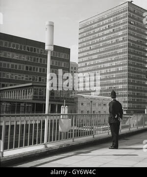 Anni sessanta, storico, poliziotto si affaccia sul nuovo moderno ed alto edificio edifici di uffici nella città di Londra, nei pressi del centro di Barbican. Foto Stock