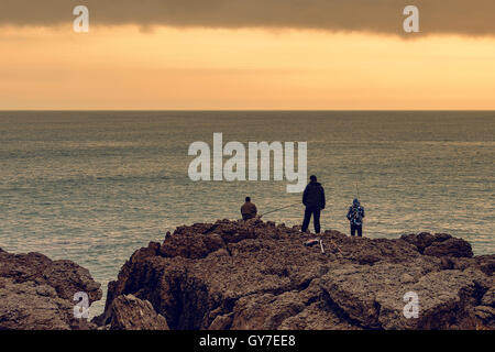Tre pescatori con le loro aste on the rocks, il fondo del mare, costiera nel nord della Cantabria, SPAGNA Foto Stock