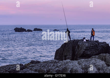 Due pescatori con le loro aste on the rocks, il fondo del mare, costiera nel nord della Cantabria, SPAGNA Foto Stock