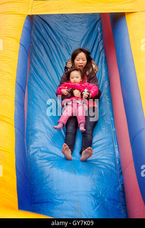 Un americano asiatico mom mantiene la sua figlia come andare giù un gonfiato il parco di divertimenti di scorrere in corrispondenza di un inverno di carnevale in Mission Viejo, CA. Foto Stock