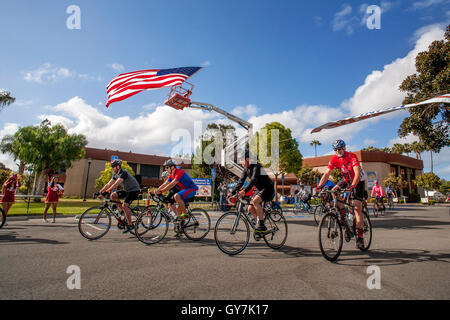 Una bandiera americana flutti nel vento come i ciclisti lascia la linea di partenza di un 55-Mile fund raising carità gara in Costa Mesa, CA. Foto Stock